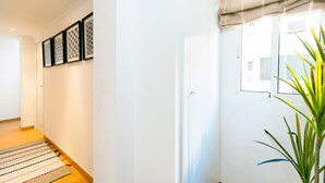 Un couloir avec un tapis à motifs, des œuvres d’art encadrées accrochées au mur et une plante en pot.