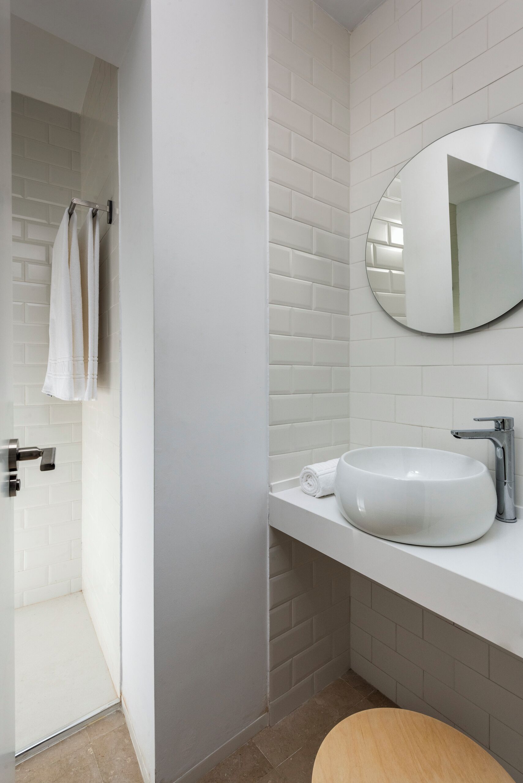 A modern bathroom with white subway tiles, a round mirror, a white sink, and a shower area.