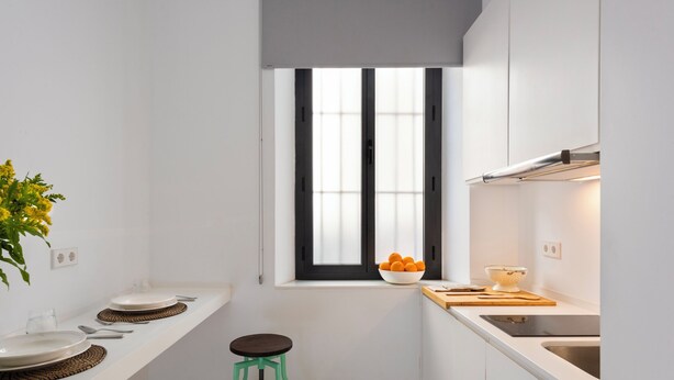 A compact kitchen with a window, white cabinets, two stools, and a bowl of oranges on the counter. - Cozy Studio in Santa Cruz Quarter Santa Teresa I (Seville)