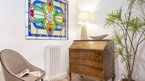 A room with a wooden dresser, a chair with a magazine, a lamp, a radiator, and a potted plant. - Cozy Apartment Near City Center Lope de Vega (Granada)