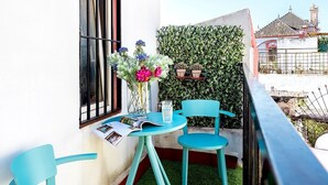 Een balkon met een tafel, stoelen, een bloevas en een raam met gordijnen.