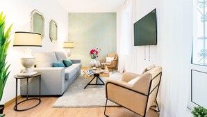 Een moderne woonkamer met een bank, fauteuils, een salontafel en een aan de muur bevestigde televisie.