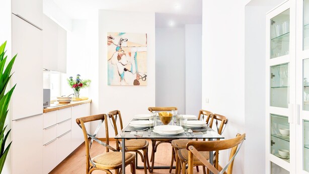 Een moderne eetruimte met een glazen tafel, houten stoelen en een witte kast met glazen deuren.