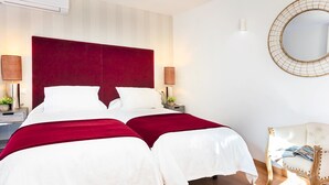 Een hotelkamer met twee bedden, een rode hoofdbord, bedlampen, een ronde spiegel en een witte stoel.