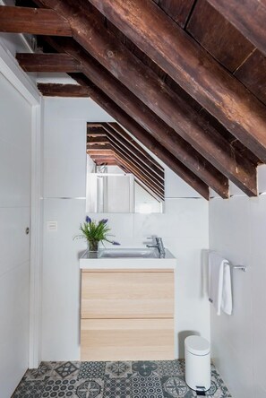 Een moderne badkamer met een houten plafond, een wastafel met spiegel, een handdoekrek en vloertegels met een patroon.