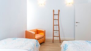 Una habitación con dos camas, una escalera de madera y dos luces fijadas a la pared.