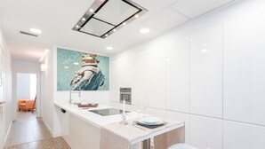 Una cocina moderna con una isla central, armarios blancos y un cuadro abstracto colorido sobre el fregadero.
