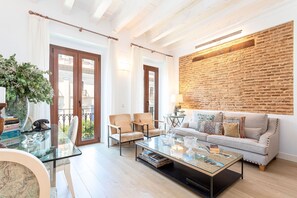 A modern living room with a glass coffee table, beige armchairs, a grey sofa with colorful cushions, and a brick wall accent. - Exclusive 2 Bedroom Apartment in the City Center Julio Cesar (Seville)