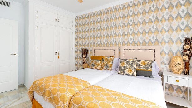 A bedroom with a bed, a nightstand, a wardrobe, and a patterned wall. - Exclusive Apartment in Front of the sea Victoria (Cádiz)