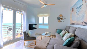A living room with a sofa, armchairs, a coffee table, and a TV. There is a balcony with a view of the sea. - Exclusive Apartment in Front of the sea Victoria (Cádiz)
