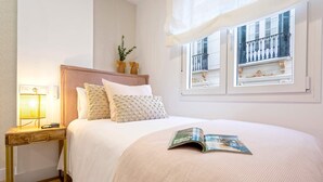 A neatly made bed with a magazine, a bedside lamp, and a window with a balcony view. - Exclusive Apartament in Malaga Center Soho (Málaga)