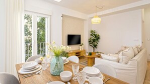 A modern living room with a dining area, a TV mounted on the wall, and a large window with curtains. - Exclusive Apartament in Malaga Center Soho (Málaga)