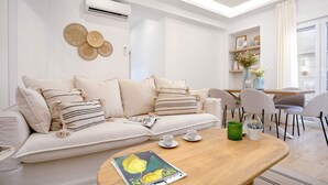 A modern living room with a beige sofa, a wooden coffee table, and a dining area with chairs and a table. - Exclusive Apartament in Malaga Center Soho (Málaga)