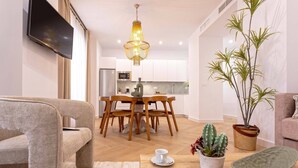 A modern living room with a sofa, a dining area with a wooden table and chairs, a kitchen in the background, and a large plant. - Exclusive Apartment in City Center Capiteles (Granada)