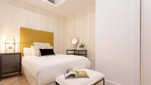 A neatly arranged bedroom with a bed, bedside tables, a reading bench, and a wall-mounted mirror. - Exclusive Apartment in City Center Capiteles (Granada)