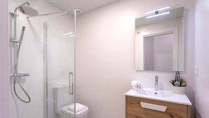 A modern bathroom with a glass-enclosed shower, a toilet, a sink with a mirror, and wooden cabinetry. - Exclusive Apartment in City Center Capiteles (Granada)