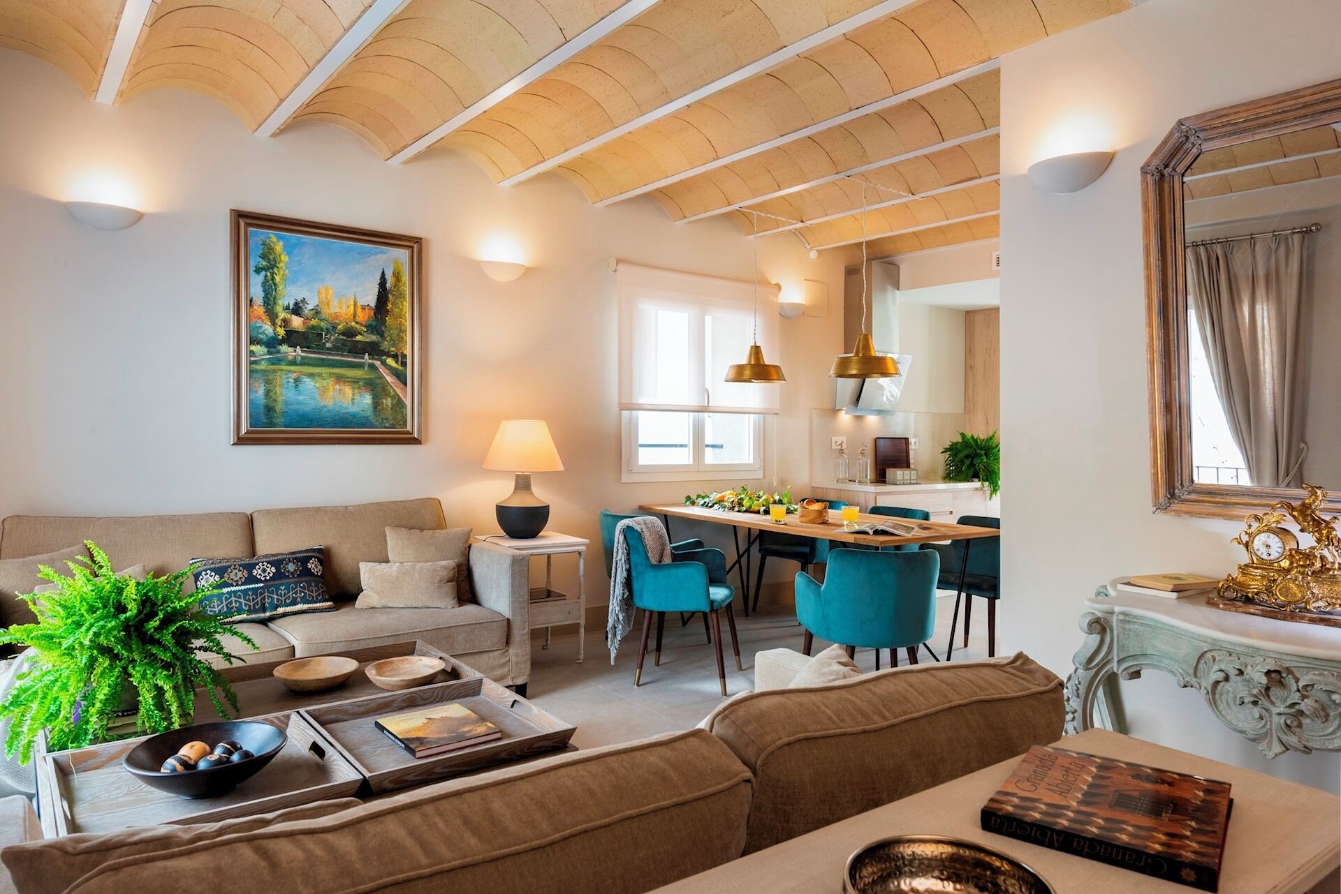 A modern living room with a sofa, a coffee table with books and decorative items, a dining area with blue chairs, and a kitchen with a dining table.