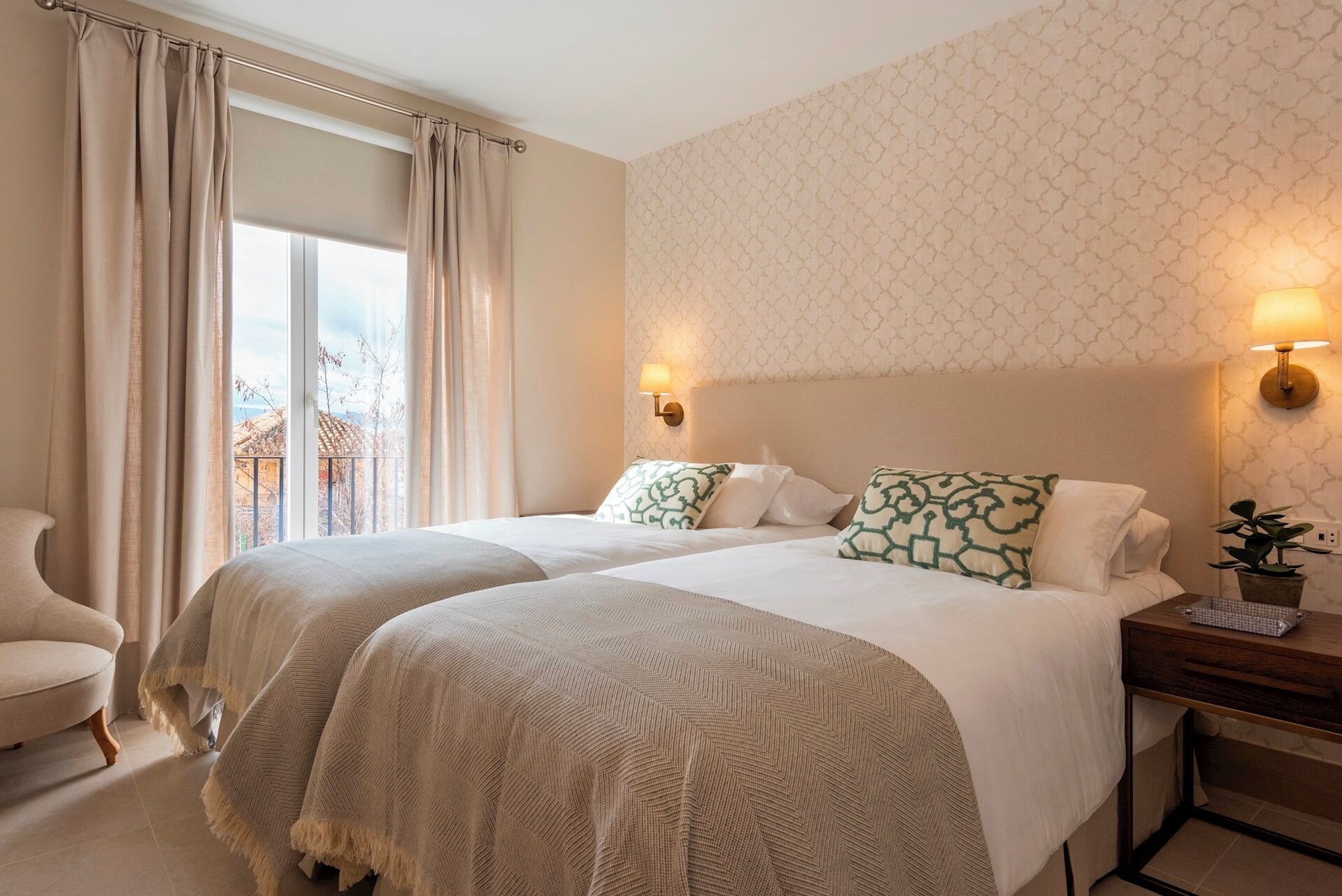 Ein Hotelzimmer mit zwei Betten, einem Sessel, einem Nachttisch und Blick ins Freie.