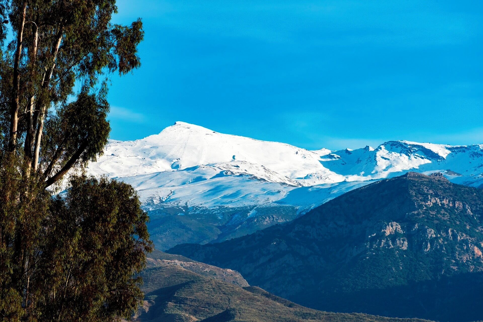A mountain landscape with snow-covered peaks and a clear blue sky.