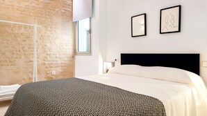 Ein Schlafzimmer mit einem gemusterten Bettbezug, einer Ziegelwand und zwei gerahmten Kunstwerken an der Wand.