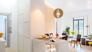 Eine moderne Küche mit weißen Schränken, einem Essbereich mit Glastisch und einem Wohnbereich mit Sofa und Lampe.
