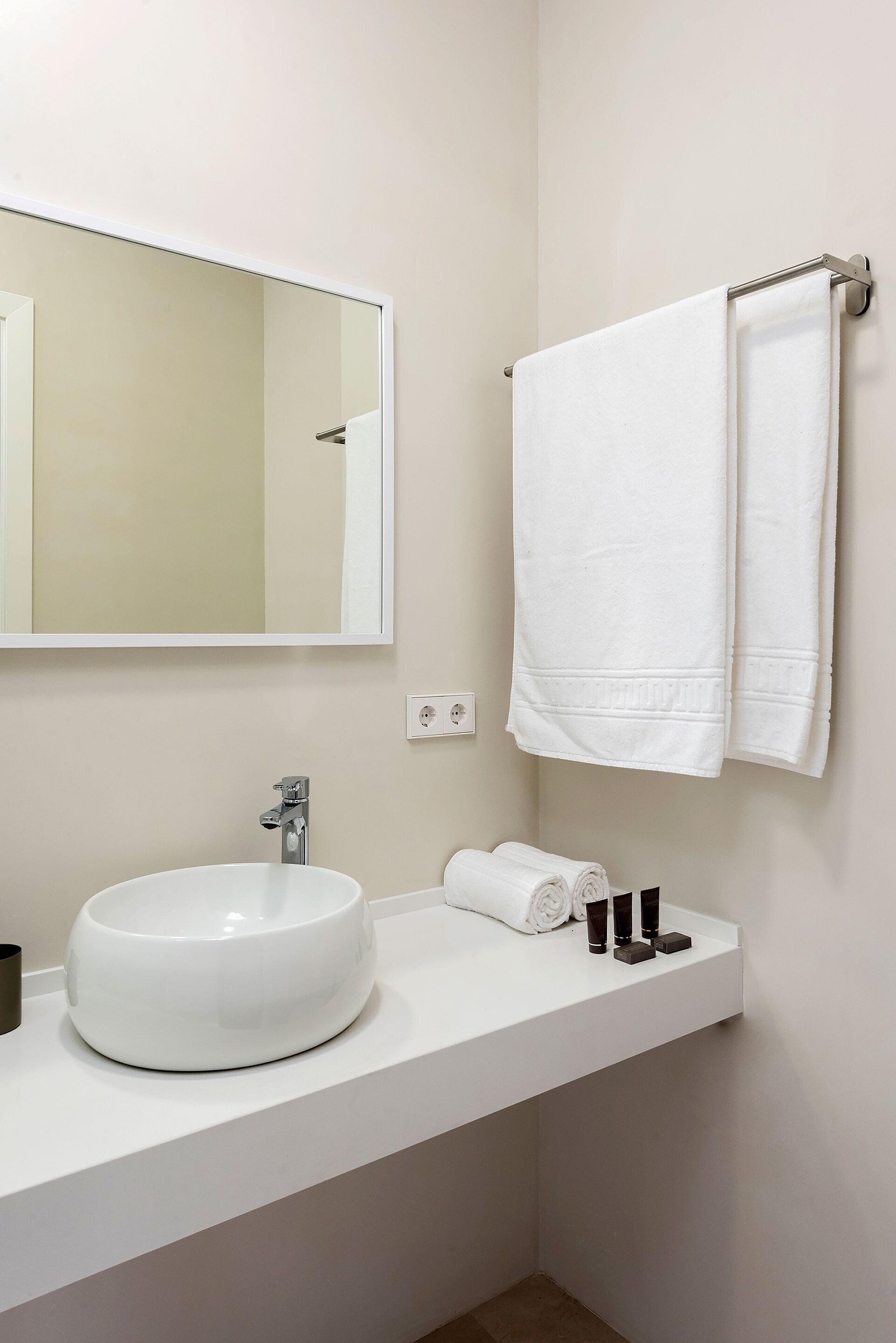 Une salle de bain avec un lavabo blanc, un miroir et deux serviettes suspendues à un porte-serviettes.