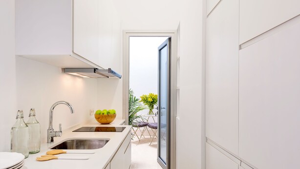 Eine moderne Küche mit weißen Schränken, einer Edelstahlspüle und einer Holzarbeitsplatte. Auf der Arbeitsplatte steht eine Schüssel mit grünen Äpfeln und eine Vase mit gelben Blumen.