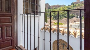 Un balcón con baranda de hierro forjado, una puerta de madera y vistas de un paisaje urbano histórico con edificios y un castillo.