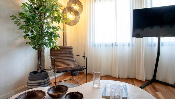 Un salón con sofá, televisión, planta y una mesa con cuencos y una revista.