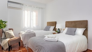 Ett hotellrum med två sängar, en stol, en växt och en luftkonditioneringsanläggning.
