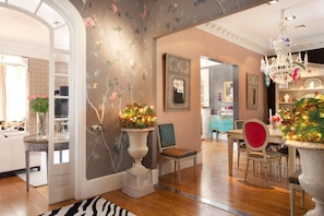 A spacious room with a wooden floor, a dining area with a red chair, and a chandelier.