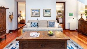 Ein Wohnzimmer mit einer Couch, einem Couchtisch und einer Zeitschrift. An den Wänden befinden sich gerahmte Bilder und ein Holzschrank.