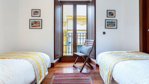 Ein Schlafzimmer mit zwei Betten, einem Sessel und einem Balkon mit gelben Geländern.