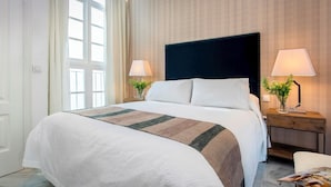 Een hotelkamer met een groot bed, twee nachtkastjes met lampen, een raam met gordijnen, en houten wandbekleding.