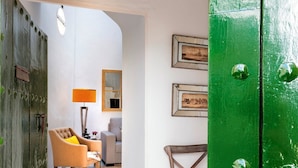 Een kamer met een groene deur, een rond geweven vloerkleed, een houten stoel, een bank, een lamp en een ingelijst schilderij aan de muur.