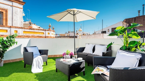 Een terras op het dak met rieten meubels, een tafel en een parasol.