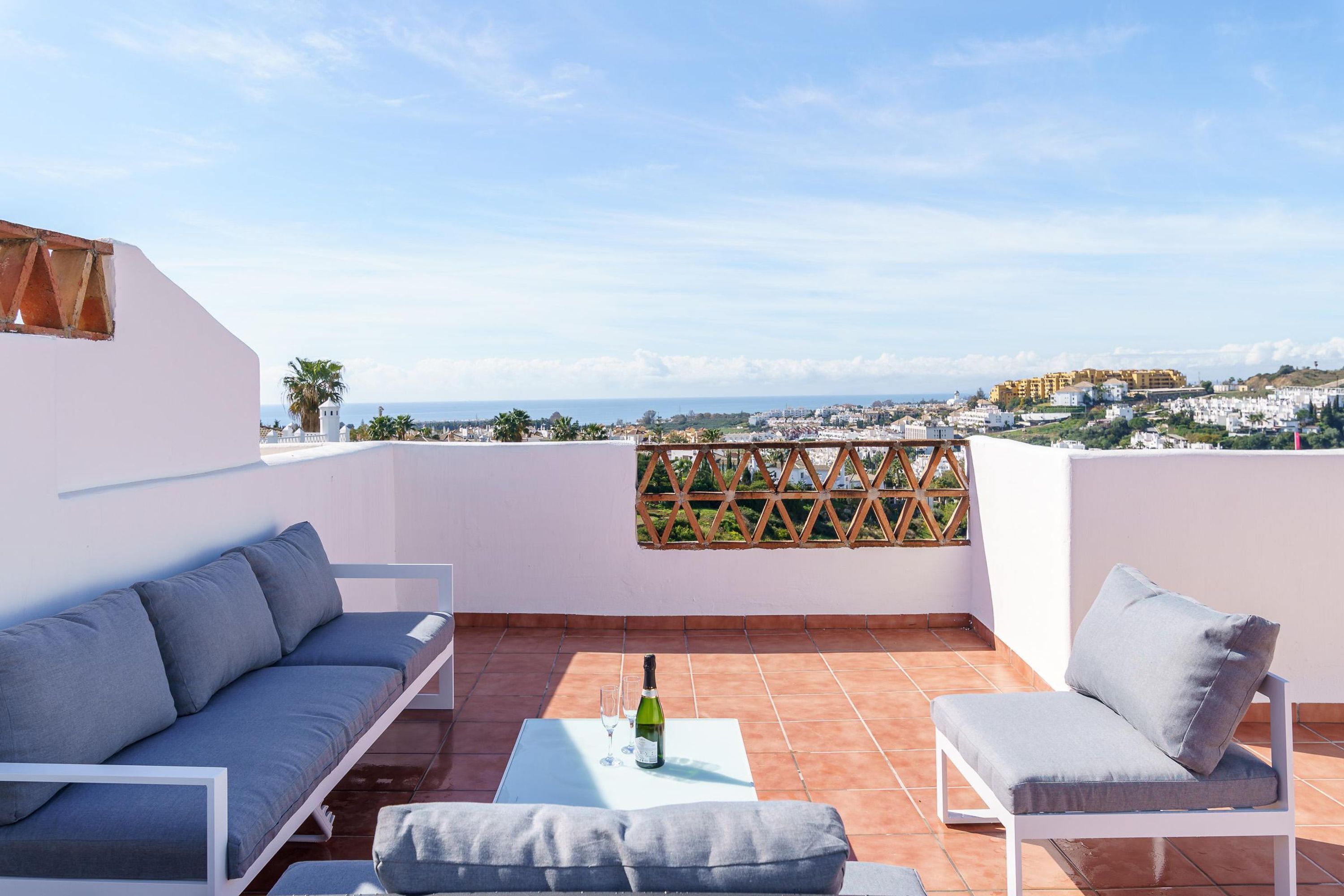 Una terrazza con un divano, una poltrona e un tavolo con una bottiglia e un bicchiere.
