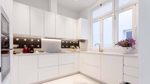 A modern kitchen with white cabinets, a black backsplash with star patterns, a red kettle, and a window with a flower vase. - Luxury Apartment in Malaga Beach Paseo Mar Timo (Málaga)