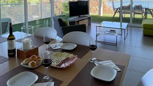 A dining area with a table set for two, a television in the background, and a view of the sea through large windows. - Luxury Apartment With Sea View (Benalmádena)
