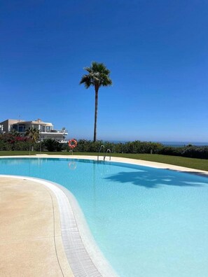 A clear blue swimming pool with a palm tree and a building in the background. - Luxury Apartment With Sea View (Benalmádena)