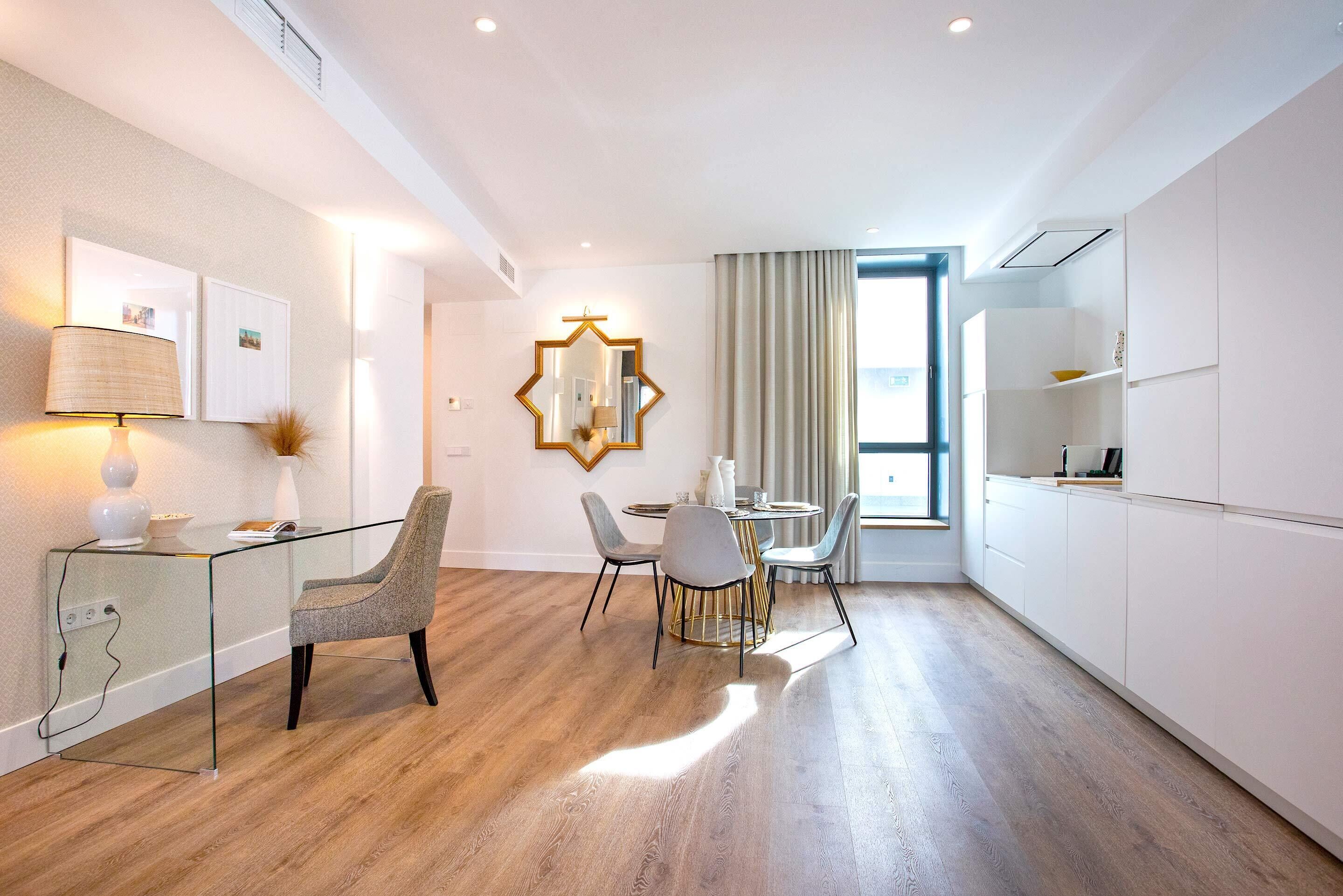 A modern hotel room with a glass desk, two chairs, a round table, and a large mirror on the wall.