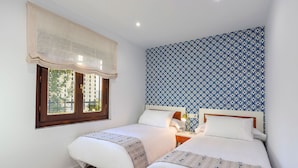 Een slaapkamer met twee bedden, een raam met gordijn en een behang met patroon.
