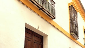 Un edificio con una puerta de madera grande, un ventanal con barrotes de metal y un balcón con barandilla metálica.