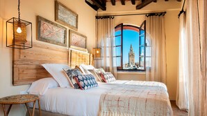 Un dormitorio con una cama grande, cabecera de madera, vista a un edificio histórico y una lámpara colgante.