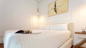 Uma cama bem arrumada com uma revista, um quadro na parede e uma mesa de cabeceira de madeira.