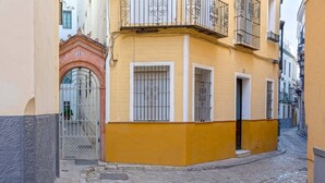 Uma rua de paralelepípedos estreita, ladeada por edifícios com janelas protegidas por grades e um arco vermelho.