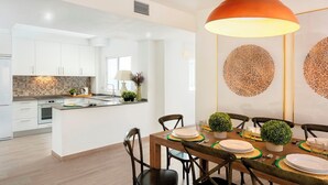 A modern kitchen with white cabinets, a central island, and a dining area with a wooden table set for six. - Magnificent 3 Bd 2 Bathrooms in Plaza de las Flores (Málaga)