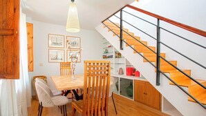 A dining area with a wooden table and chairs, a staircase with a glass railing, and framed pictures on the wall. - Modern Confortable 3 Bd Duplex Great Location Piedra Santa (Granada)