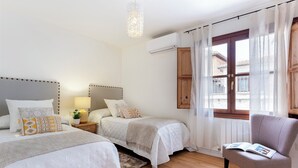A bedroom with two beds, a chair, a nightstand, a lamp, and a window with curtains. - Modern Confortable 3 Bd Duplex Great Location Piedra Santa (Granada)