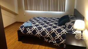 Een slaapkamer met een bed, een nachtkastje met een lamp, een raam met zonwering en een houten vloer.
